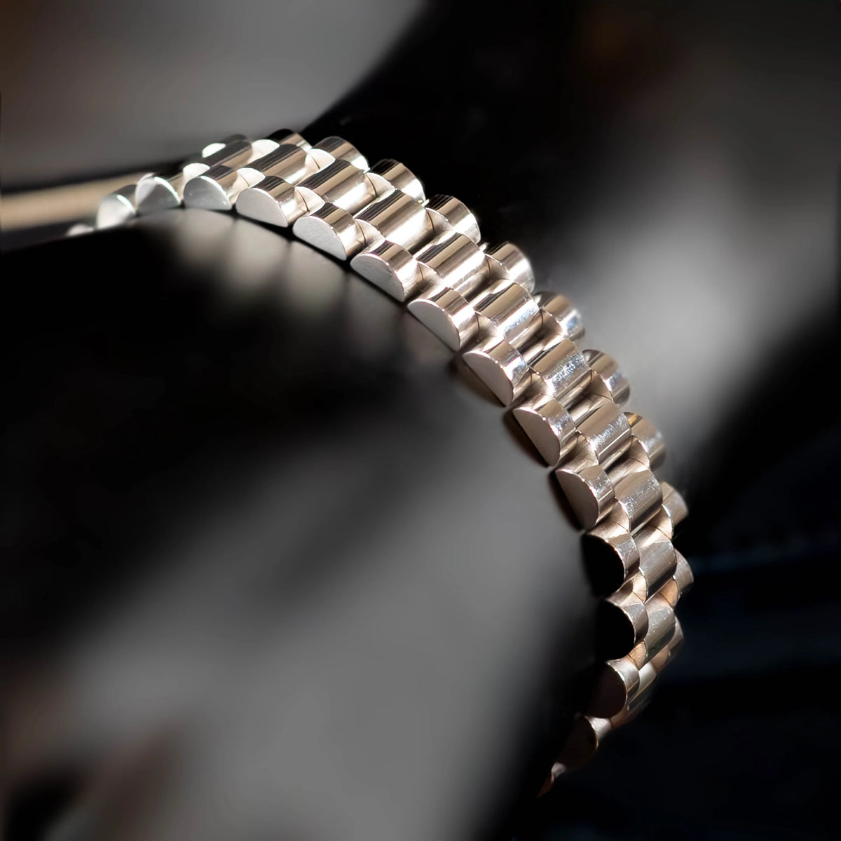 Metal watch bracelet with a curved, segmented design.