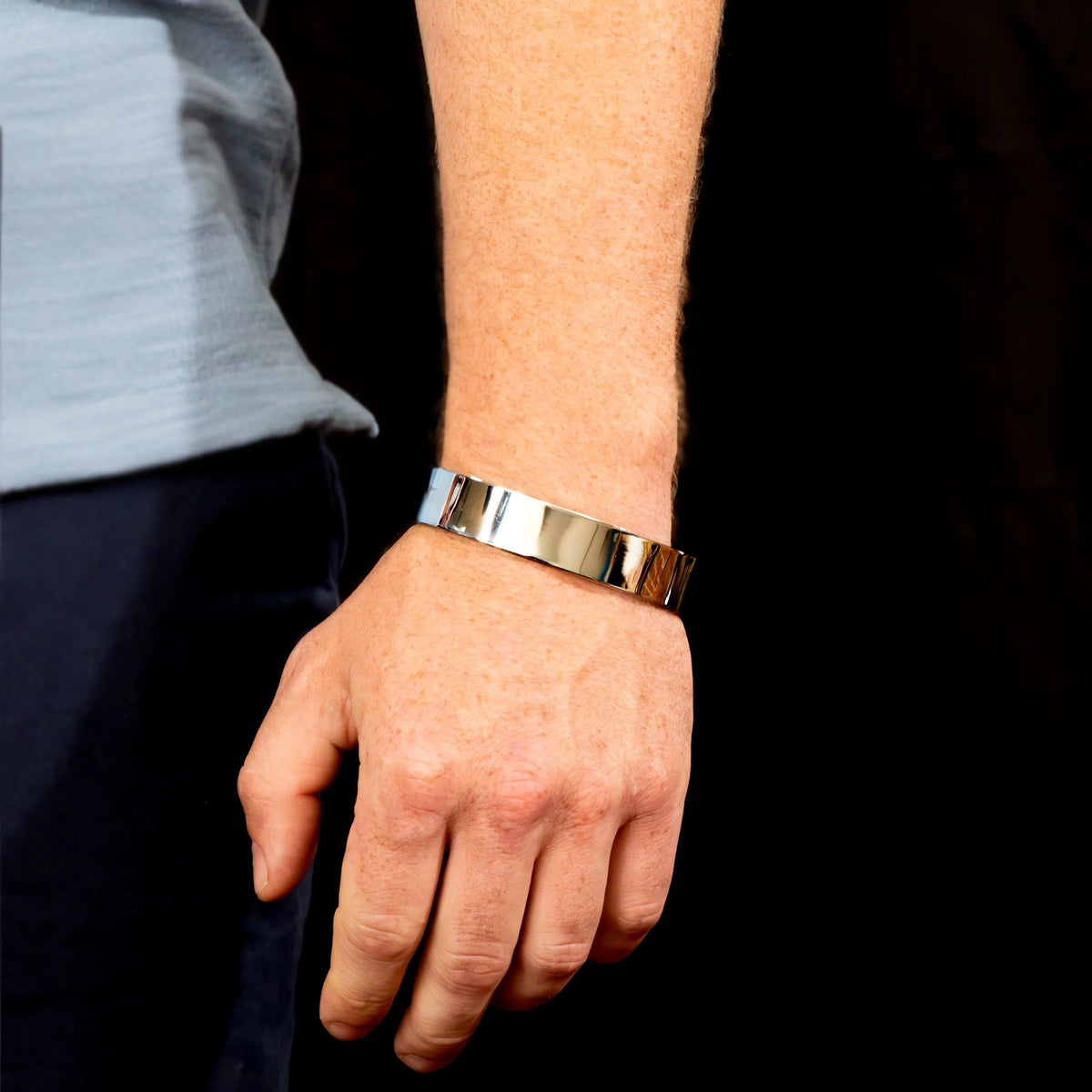 Metallic silver bracelet with a wide band worn on a wrist.