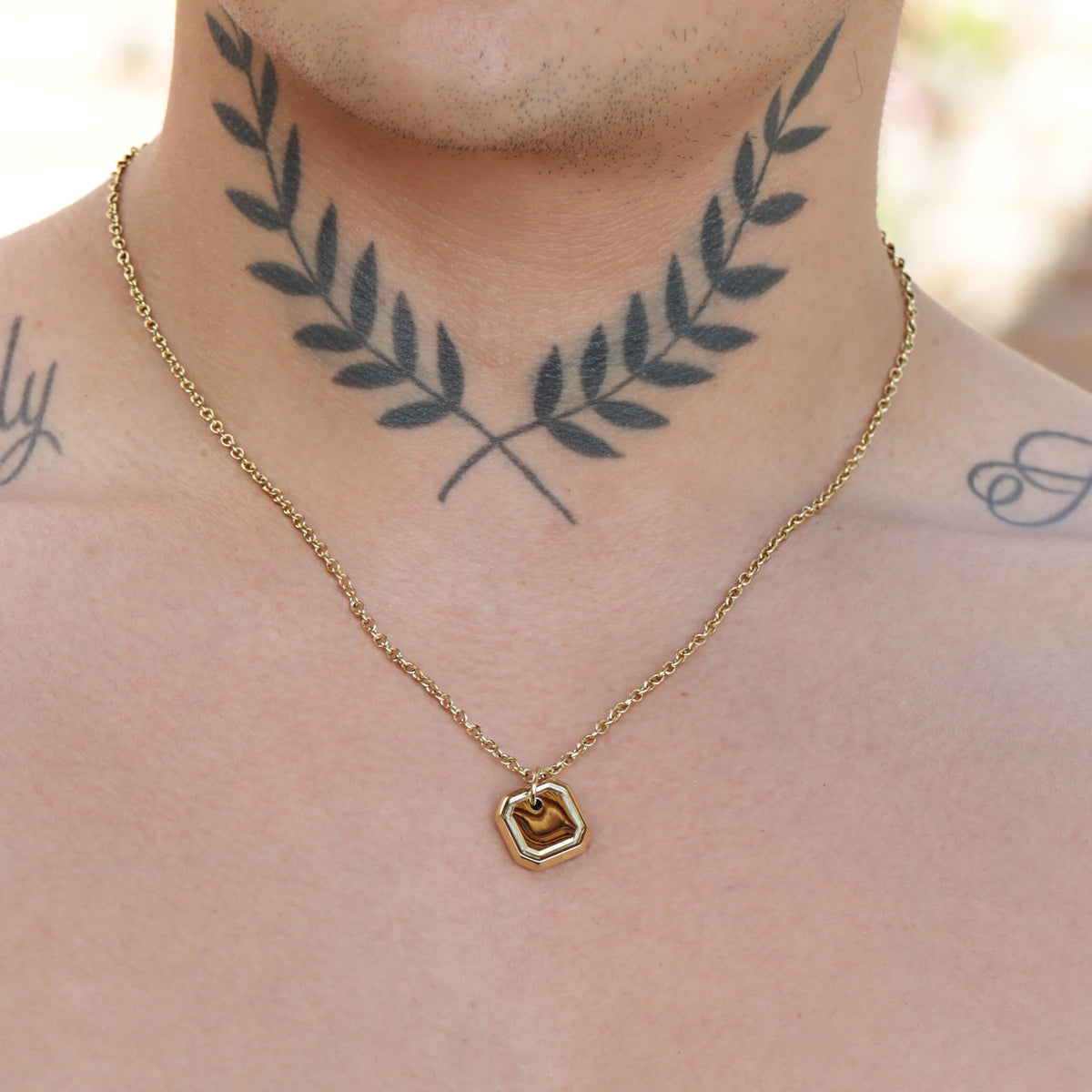 Tattoo of symmetrical laurel branches on a person’s neck.